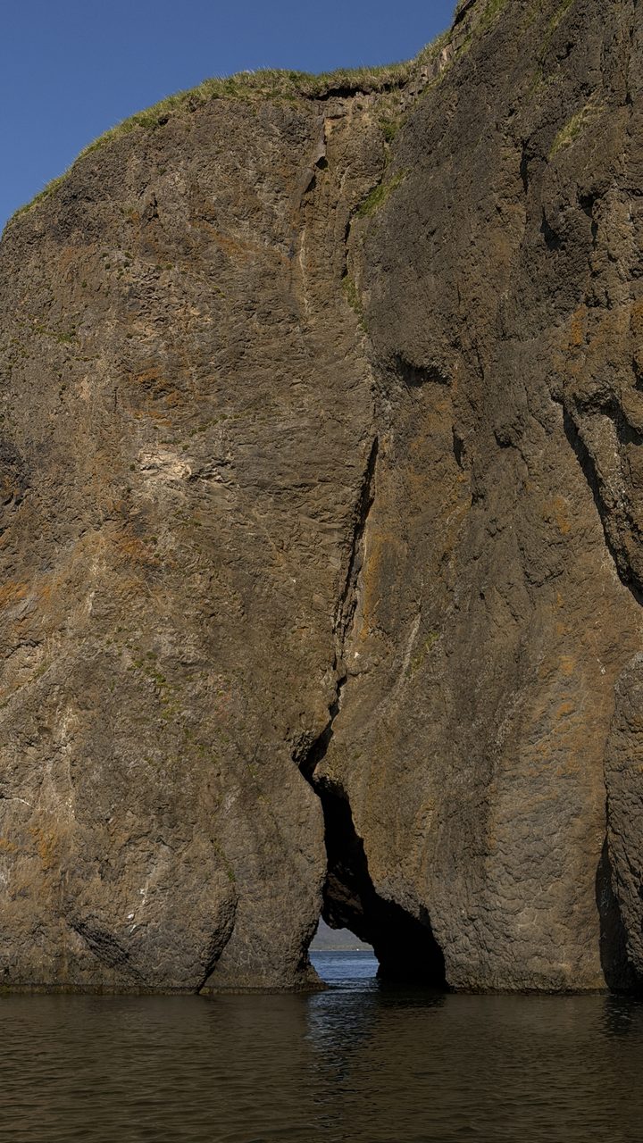 Tall coastal cliff with a grotto at the waterline in Kamchatka